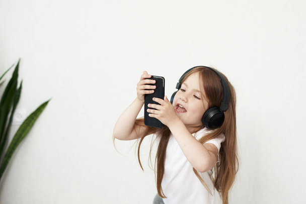 Dziewczynka bawi się telefonem w tle. Dziewczynka w słuchawkach. Dziewczyna słucha muzyki.. - Zdjęcie, obraz