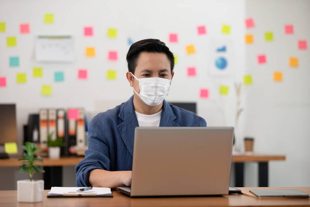 Asian senior business man in casual wearing mask working with laptop in modern office or co-working space Due Covid-19 Flu Pandemic,Health care and Business Startup Concept - Фото, изображение