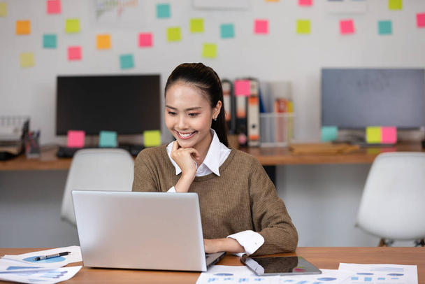 Happy Asian business woman in casual working with laptop and smile looking at camera at modern office or Co-Working Space,Business Startup Concept - Zdjęcie, obraz