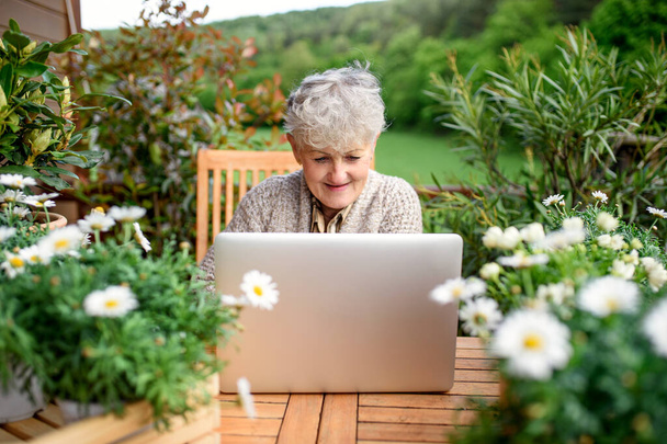 Senior woman with laptop sitting on terrace in summer, resting. - Fotografie, Obrázek