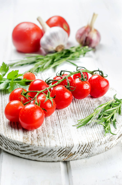Bunch of juicy organic red cherry tomatoes with green  rosemary,  garlic and spices on white old table. Ingredients for cooking. Clean eating concept. Vegetarian diet. space for text - Foto, Imagem