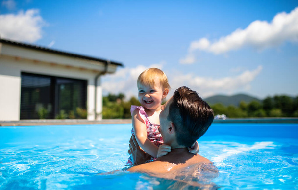 Young father with small daughter in swimming pool outdoors in backyard garden. - Foto, Imagem