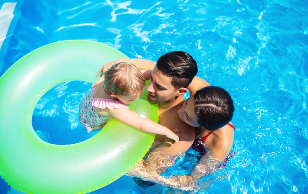 Top view of young family with small daughter in swimming pool outdoors. - Foto, imagen