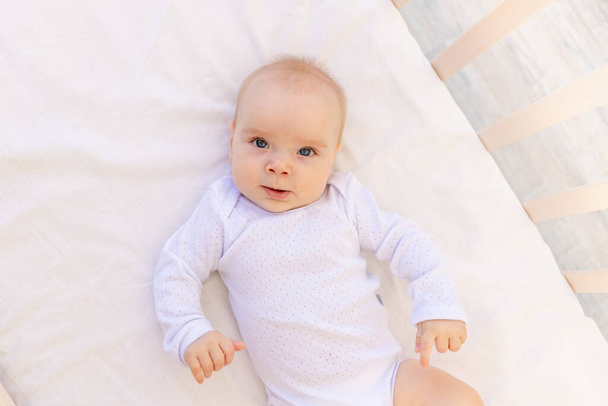小さな赤ん坊の女の子の肖像画6ヶ月白い体のスーツで彼女の背中に白いベッドの上に横たわる,テキストのためのスペース - 写真・画像