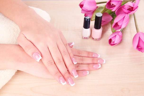 Beautiful woman hands with french manicure and flowers on wooden background - Photo, Image