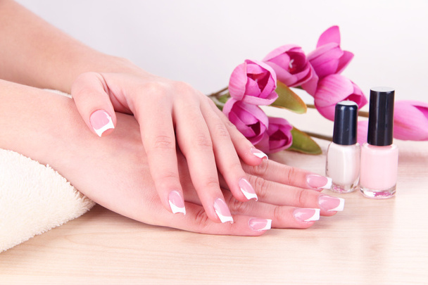 Beautiful woman hands with french manicure and flowers on table on white background - Photo, Image