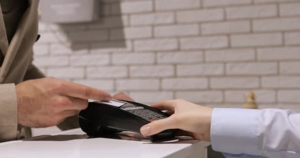 Egy férfi bankkártyát tart a kezében a terminál előtt. Fehér hitelkártya fénykép nélkül. Fizetés hitelkártyával a terminálon - Felvétel, videó