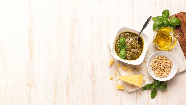 Miska z pesto i świeża bazylia, czosnek, ser parmezan, orzechy sosnowe i oliwa z oliwek na desce marmuru. Kuchnia drewniany stół z sosem włoskim - Zdjęcie, obraz