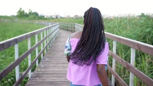Афроамериканка с кукурузниками бежит по мосту - Кадры, видео
