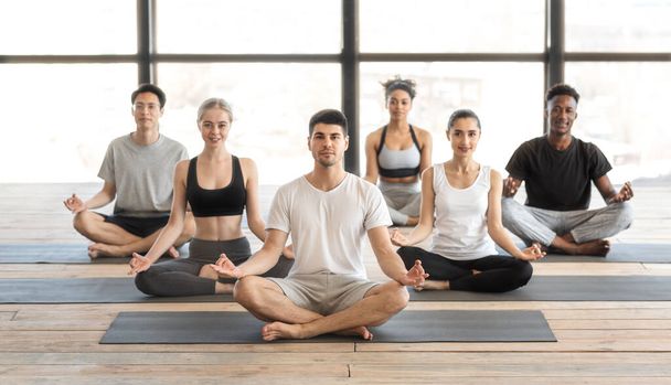 Yoga-Praxis. Lächelnde junge Sportler meditieren gemeinsam mit Coach im Studio - Foto, Bild