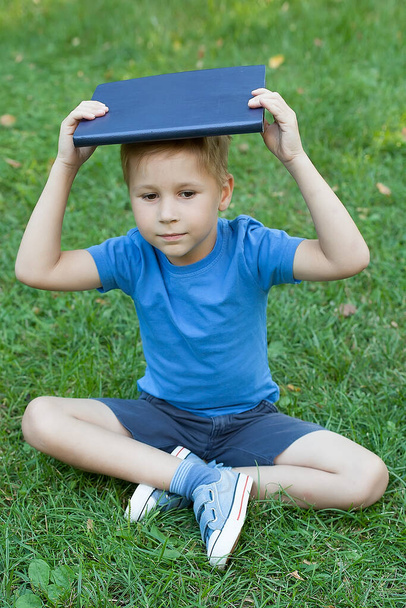 Mladý chlapec těší jeho čtení knihy ve venkovním parku - Fotografie, Obrázek