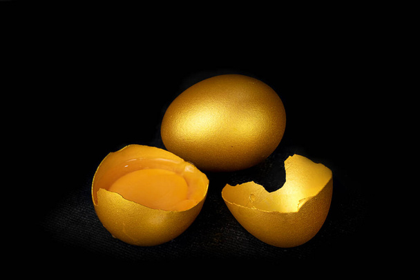 Huevos dorados y huevo medio roto con yema aislada en el fondo negro - Foto, imagen