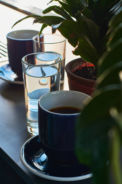 Schwarzer und kräftiger Morgenkaffee in blauen Bechern und grüne Pflanzen in Töpfen. - Foto, Bild