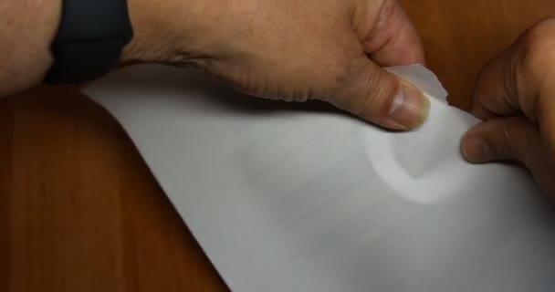 Handen scheuren een vel documenten in kleine stukjes op het bureau. - Video