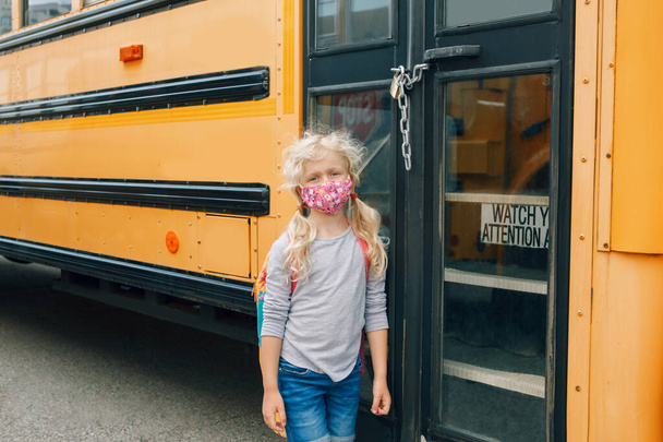 Sad girl student with face mask near locked yellow bus. Closed school during pandemic lockdown and quarantine shutdown. Education and back to school. New normal in coronavirus.  - Photo, Image