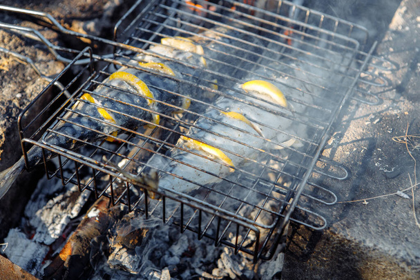 Grilled fish. Mackerel in a steel lattice turns over a brazier - Photo, Image