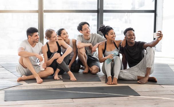 Happy yoga class members taking selfie on smartphone after training in studio - Fotó, kép
