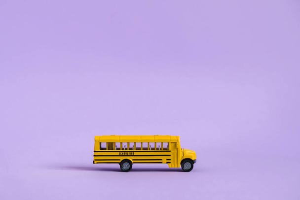 Back to school concept. Traditional yellow school bus on purple background. Transfer to school. Yellow toy model school bus. - Фото, зображення