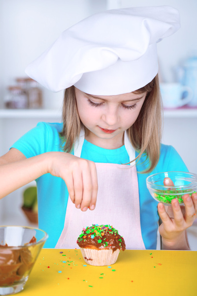 Little girl decorating cupcakes in kitchen at home - Fotó, kép