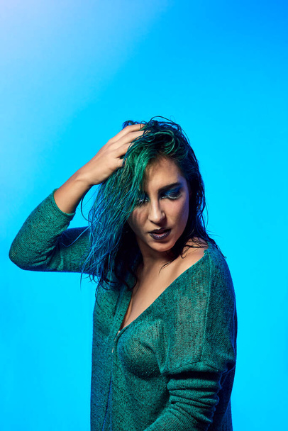 una joven con el pelo mojado posando sobre un fondo azul. Concepto de belleza y moda - Foto, imagen
