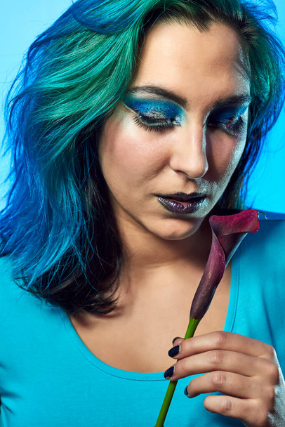 Close-up of a young woman with a flower on a blue background. Beauty and fashion concept - Photo, Image