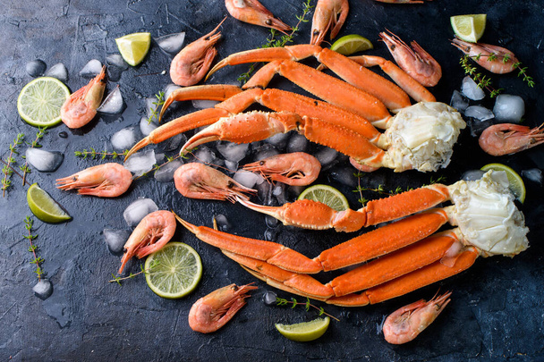 Pinces de crabe fraîches, citron vert, épices, épices, glace, crevettes, légumes sur un fond sombre. Fruits de mer délicieux, aliments sains Contenu de l'alimentation - Photo, image