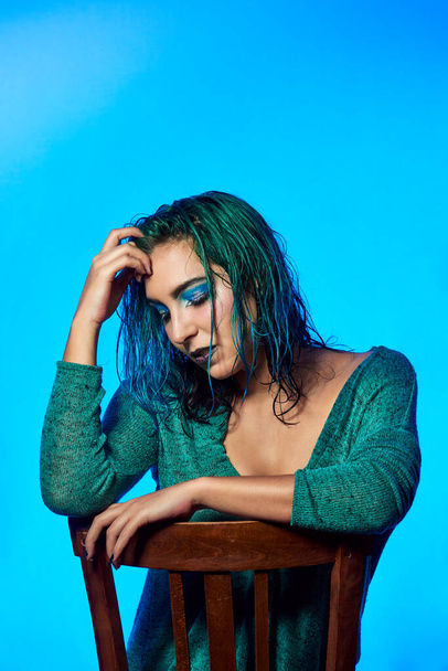 una joven con el pelo azul sentado en una silla con un fondo azul. Concepto de belleza y moda - Foto, imagen