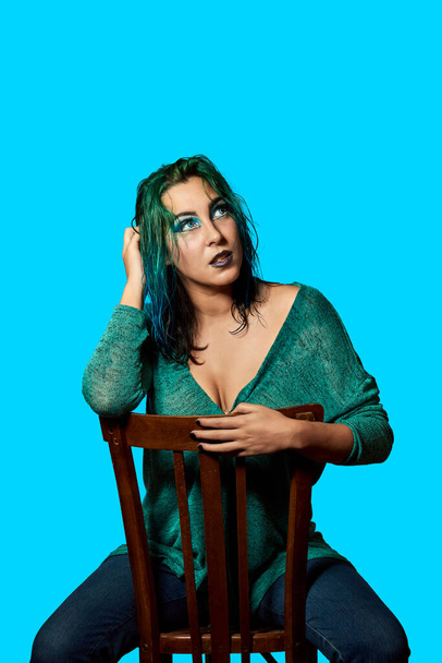 a young girl with blue hair sitting on a chair with a blue background. Beauty and fashion concept - Photo, Image