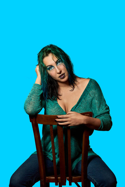 una joven con el pelo azul sentado en una silla con un fondo azul. Concepto de belleza y moda - Foto, imagen