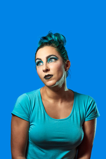 una joven con el pelo azul mirando a la derecha sobre un fondo azul. Concepto de belleza y moda - Foto, imagen
