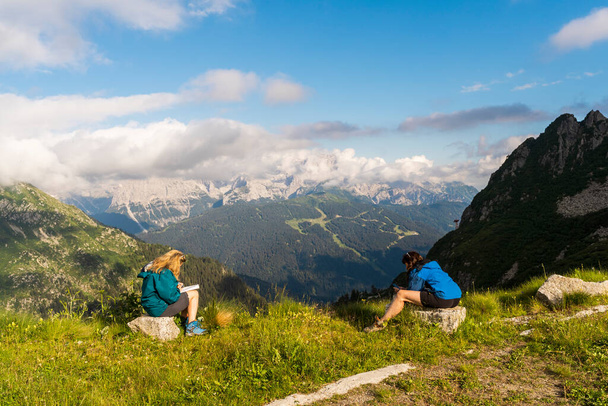 two female tourist friends are taking a break in the high mountains during a hike in the dolomites - Фото, изображение
