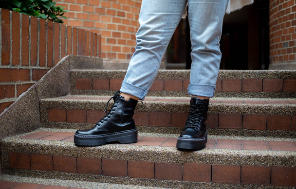 botas de cuero con jean azul, sobre fondo de calle de ladrillo, persona de pie, solo pies - Foto, imagen