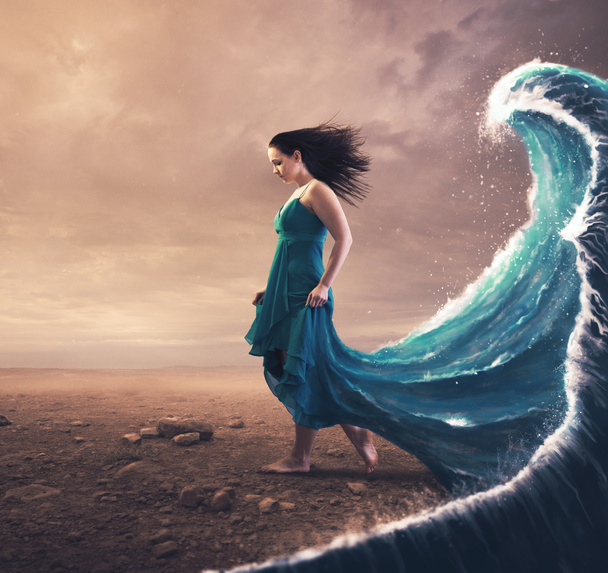 Une femme avec une robe bleue et une grande vague derrière elle. - Photo, image