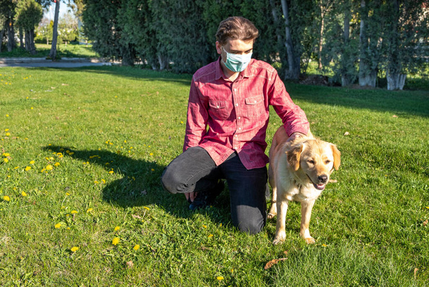 jongen draagt virus masker met zijn hond spelen in de tuin - Foto, afbeelding