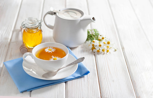 Cup of herbal tea with honey and chamomile flowers on the white wooden background. Natural alternative medicine - Photo, Image
