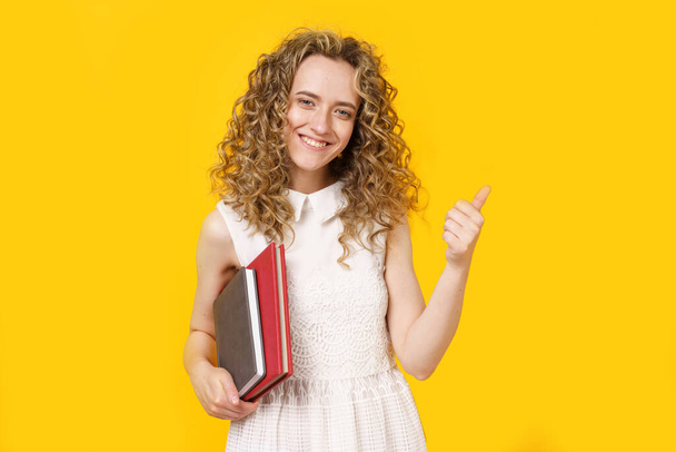 A young woman is holding a diary and a textbook. Shows gesture class. Female portrait. Isolated on yellow background - Foto, immagini