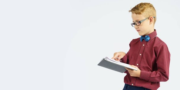 A schoolboy with glasses reads a book he holds in his hands. Isolated background. Education concept - Foto, Imagem