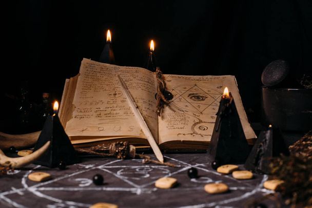 Open old book with magic spells, runes, black candles on witch table. Occult, esoteric, divination and wicca concept. Halloween vintage background - Photo, Image