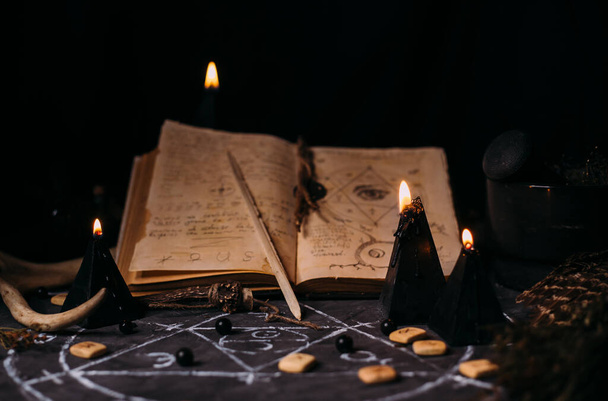 魔法の呪文、ルーン、魔女テーブルの黒いろうそくで古い本を開きます。カルト、密教、占いや魔術の概念。ハロウィンヴィンテージの背景 - 写真・画像