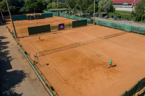 Ukraine, Kyiv- April 4, 2020: Tennis clay court seen from above with two men playing match. They are mature adult, and very agile and healthy. Video made with drone. - Фото, изображение