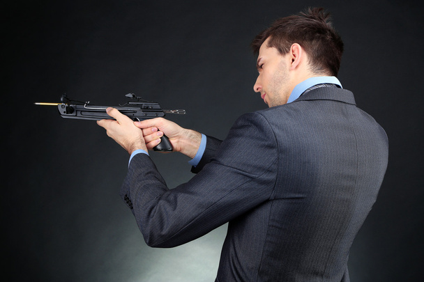 Young businessman with crossbow, on dark background - Φωτογραφία, εικόνα
