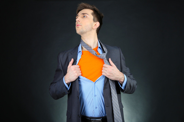 jonge zakenman scheuren naast zijn shirt onthullen superheld pak, op donkere achtergrond - Foto, afbeelding