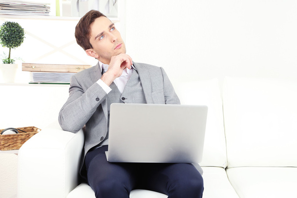 Young businessman using laptop on sofa at home - Valokuva, kuva
