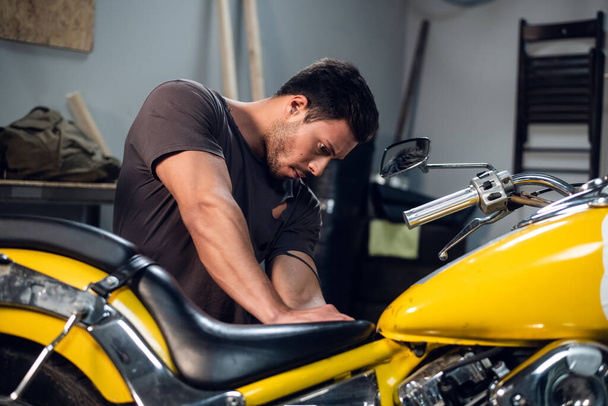 Ein moderner junger Mann in T-Shirt und Jeans ist in einer Werkstatt oder Garage mit der Fahrraddiagnostik beschäftigt. - Foto, Bild