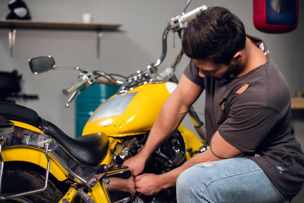 Private vehicle repair shop. Tuning a yellow chopper by a young mechanic. - Photo, Image