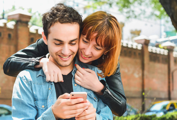 Portrait of young couple having fun and using mobile phone outdoors at the street. Relationship and technology concept. - Φωτογραφία, εικόνα