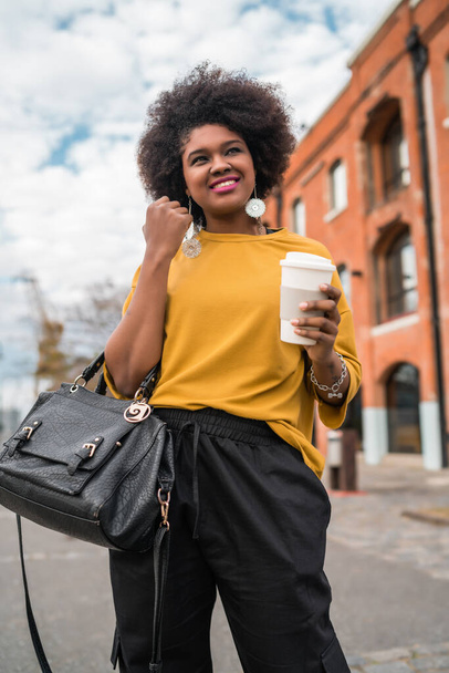 Portrait of beautiful afro american latin woman walking and holding a cup of coffee outdoors in the street. Urban concept. - Foto, Imagen