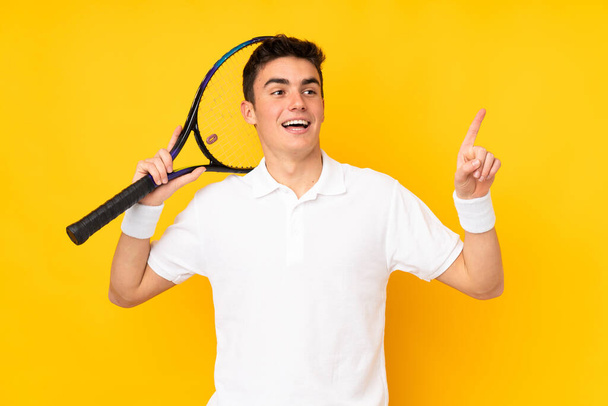 Przystojny nastolatek tenisista człowiek izolowany na żółtym tle gra w tenisa i wskazując w górę - Zdjęcie, obraz