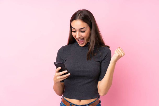 Menina sobre fundo rosa isolado surpreendido e enviando uma mensagem - Foto, Imagem