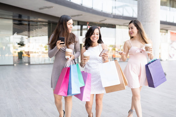 Amigos alegres usando smartphones enquanto carregam sacos de compras - Foto, Imagem